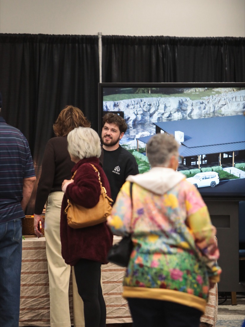 Visitors listening to an exhibitor in front of a large screen showing a home design